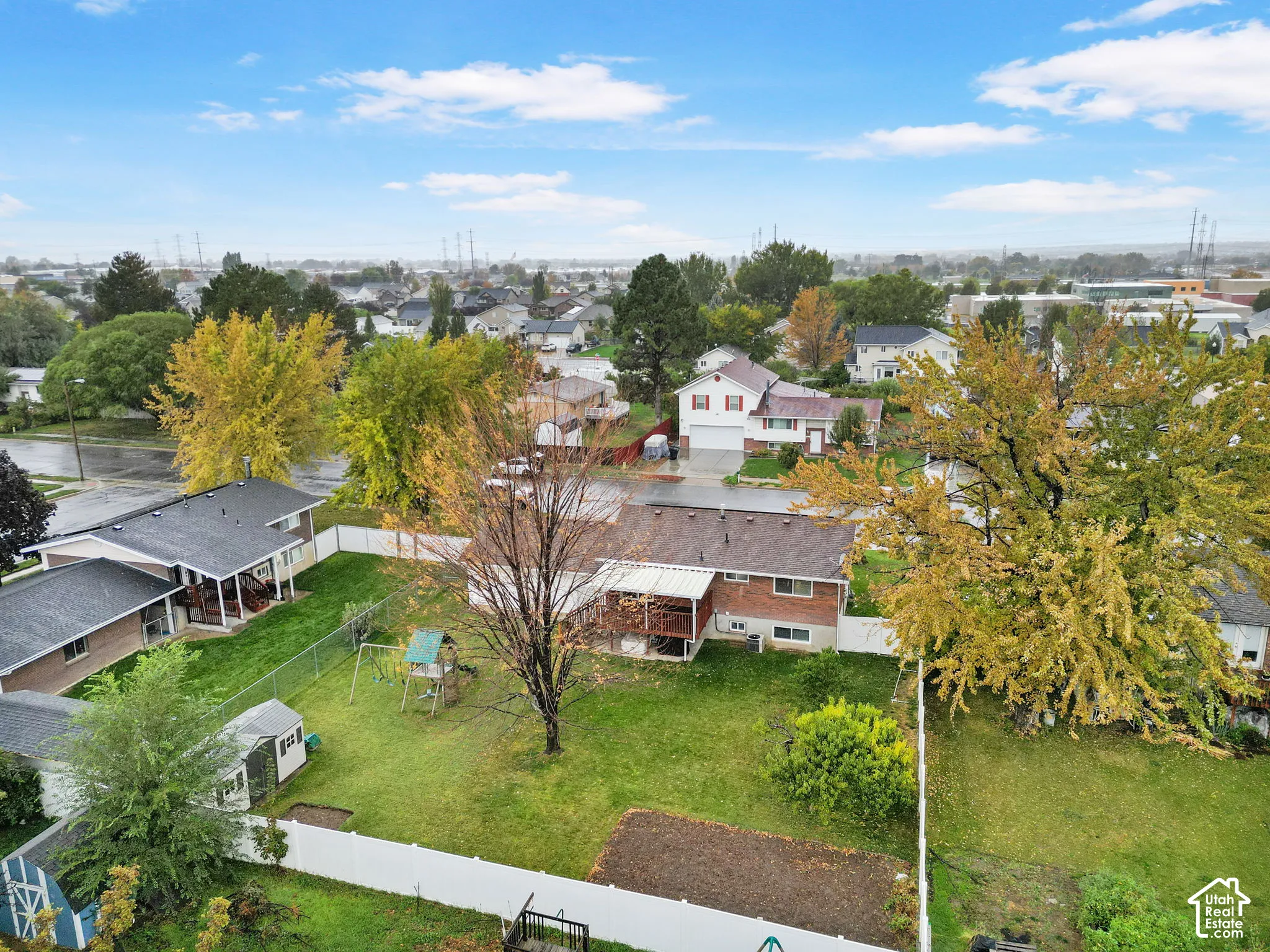 Fenced backyard featuring a raised wooden deck, mature trees, lawn area, and a detached storage structure