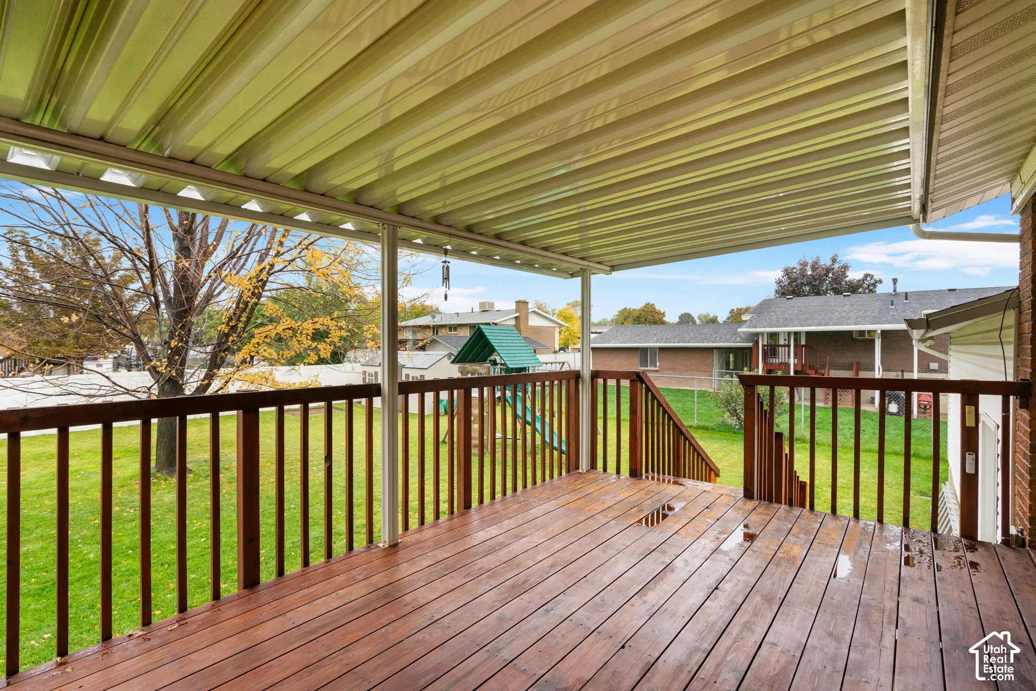 Covered outdoor deck featuring wood decking, wood railing, and a corrugated metal patio cover