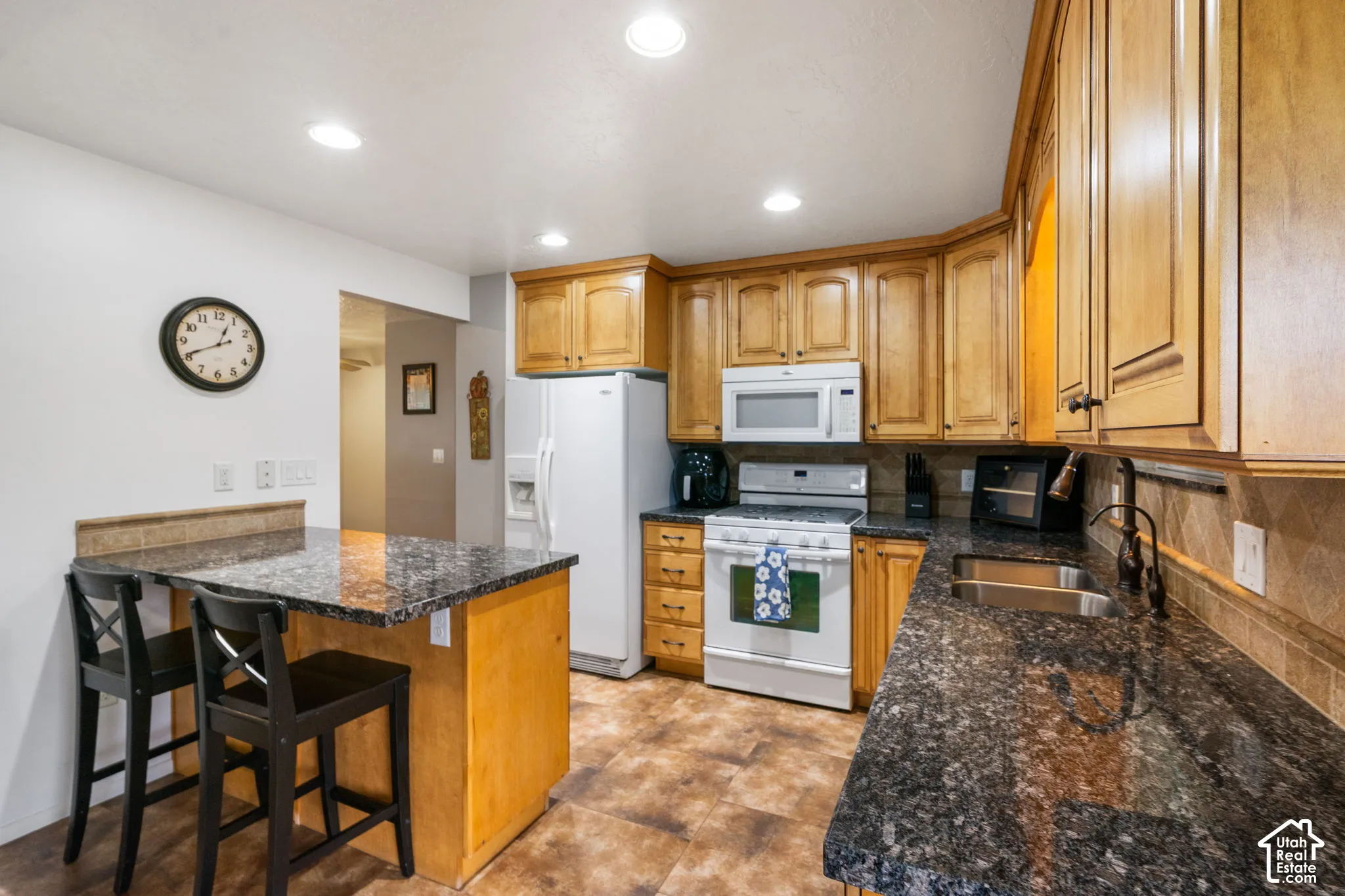 Kitchen featuring wood cabinetry, stone countertops, an integrated breakfast bar, recessed lighting, and tile flooring