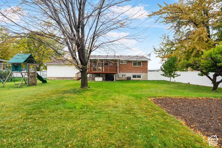 Rear exterior featuring brick siding, a raised wooden deck, a partially fenced perimeter, and mature trees