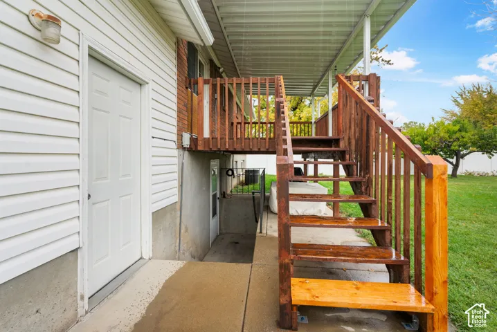 Exterior staircase with stained wood finish and railings, elevated deck with overhead covering, concrete lower-level walkout entrance, and horizontal siding