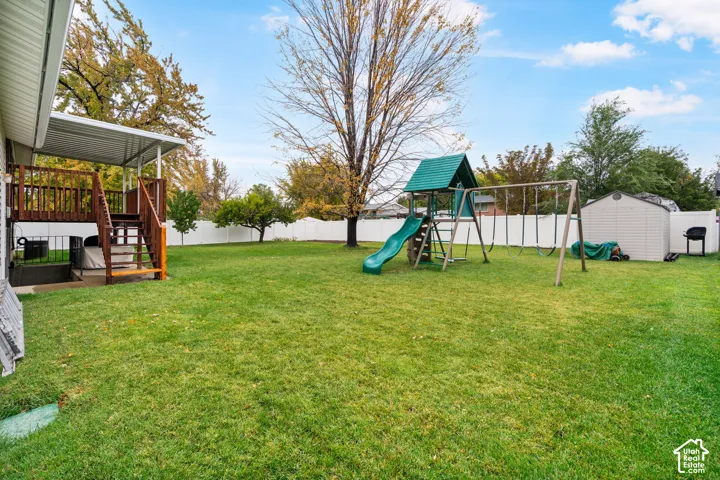 Fenced backyard featuring an elevated wooden deck with a covered patio, a detached storage shed, and mature trees