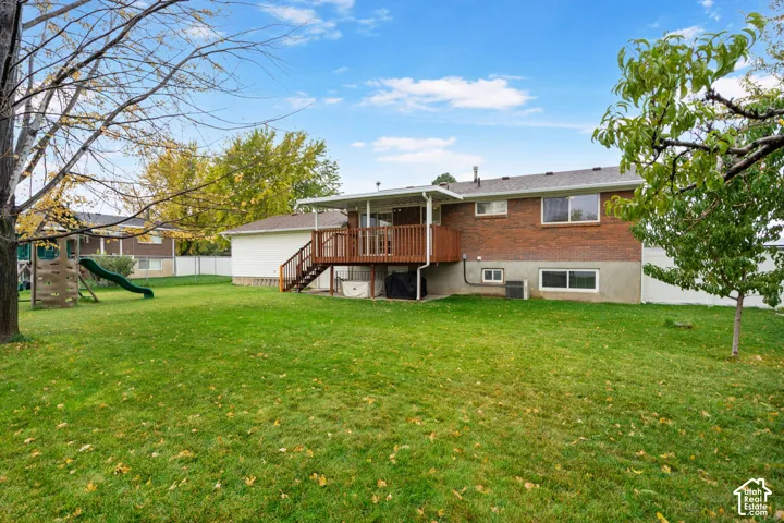 Expansive backyard featuring a large grass lawn, mature trees, and a wooden deck with railing
