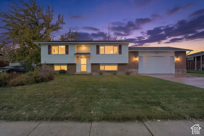 Split-level exterior featuring white siding, brick masonry, an attached two-car garage, and an expansive front lawn