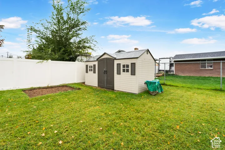 Backyard space featuring a detached storage shed, white vinyl privacy fencing, chain-link perimeter fencing, and a dedicated garden bed