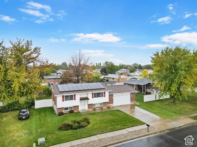 Split-level exterior featuring a brick and siding facade, solar panel array, attached two-car garage, concrete driveway, and white vinyl privacy fencing