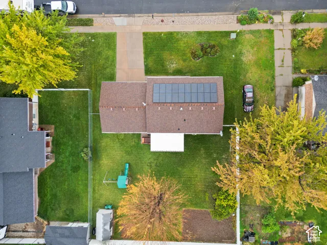 Aerial perspective of a property featuring solar panels, a paved driveway, a fenced backyard, and mature trees