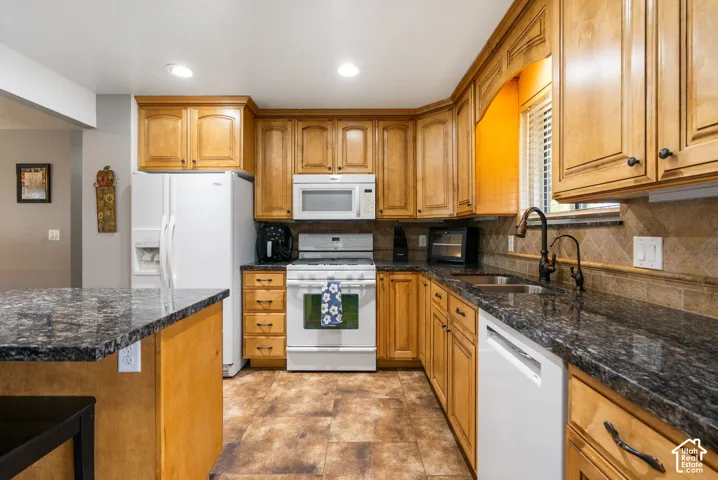 Kitchen featuring warm-tone wood cabinetry, dark stone-finish countertops, tile backsplash, recessed lighting, and built-in appliances