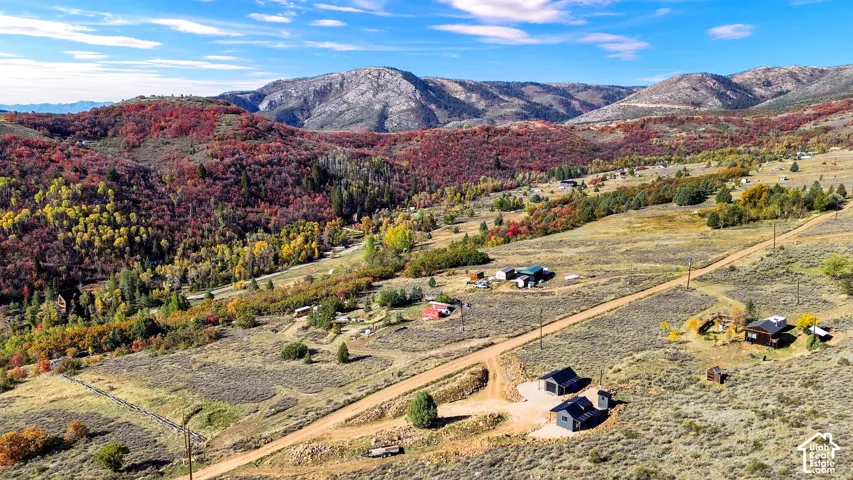 Expansive mountain landscape with diverse foliage, featuring multiple structures and a dirt road network