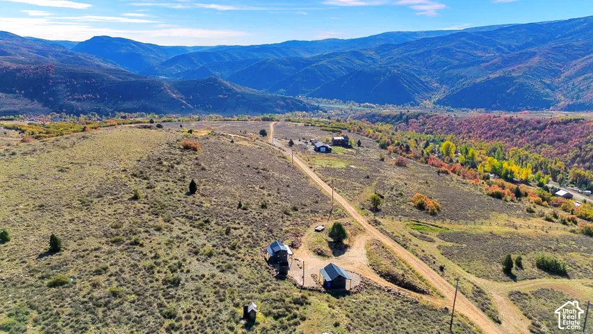 Expansive mountainous terrain featuring a dirt road, multiple structures, and varied foliage