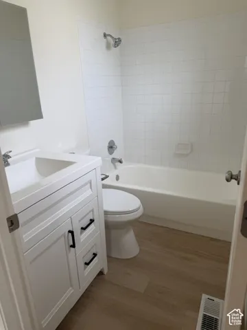 Master bathroom White vanity with shaker-style cabinetry, square integrated sink, wood-finish flooring, and white square wall tiling surrounding the tub