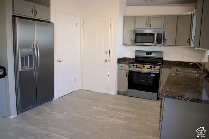 Kitchen featuring stainless steel appliances, grey cabinetry, dark countertops, and tile flooring