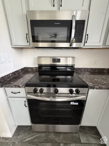 Both NEW Stainless steel freestanding electric range with smooth cooktop and matching over-the-range microwave, set within white cabinetry and stone-finish countertops