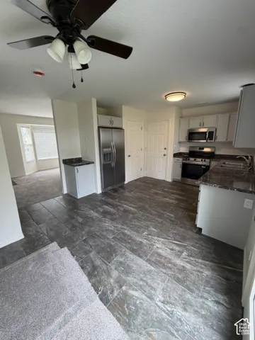 Kitchen featuring tile flooring, stone-finish countertops, stainless steel appliances, white cabinetry, and a ceiling fan with integrated lighting