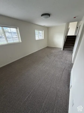 Neutral-toned interior space featuring carpeted flooring, two windows with horizontal blinds, and a built-in staircase with carpeted treads