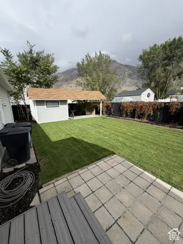Backyard featuring a paved stone patio, manicured lawn, detached storage structure with a covered porch, and mountain backdrop