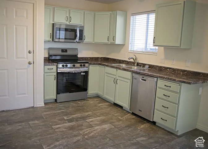Kitchen featuring light green cabinetry, dark patterned countertops, stainless steel appliances, and tile flooring