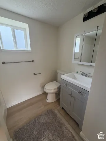 Grey shaker-style vanity with integrated sink, tri-panel medicine cabinet, multi-bulb wall-mounted vanity light, and wood-finish flooring