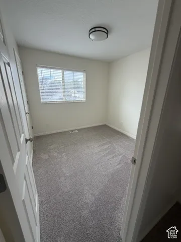 Neutral interior room featuring neutral-toned carpeting, a window with installed horizontal blinds, and a circular flush-mount ceiling light fixture