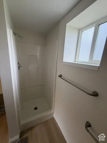 White acrylic shower surround with a polished chrome shower head, wood-finish flooring, privacy-glass window, and brushed-nickel hardware