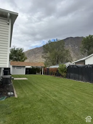 Backyard featuring a manicured lawn, detached storage structure, perimeter privacy fencing, and mountain backdrop