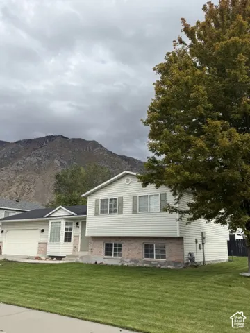 Split-level exterior featuring horizontal siding, masonry lower-level accents, an attached two-car garage, and a mountain backdrop