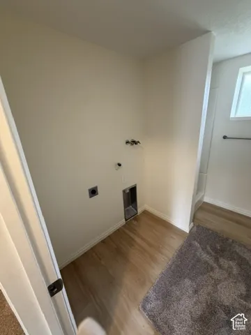 Dedicated utility area featuring wood-finish flooring, recessed water supply valves, and a grounded electrical outlet Laundry/bathroom