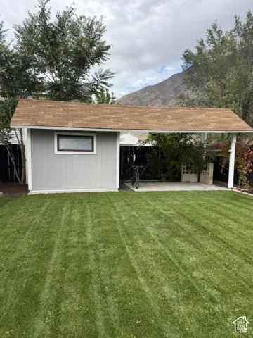Backyard structure with shingled gable roof, attached open-air carport, horizontal siding, and grass lawn