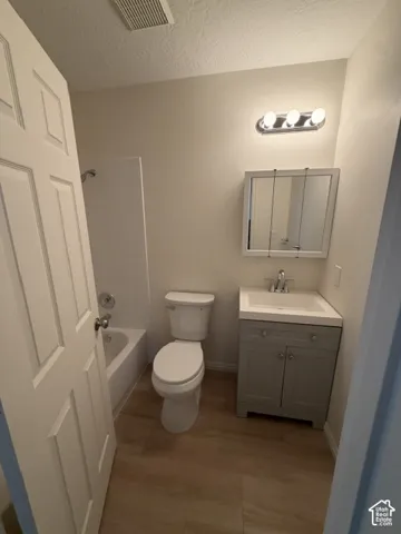 Hall Bathroom featuring wood-  flooring, a grey vanity with a square sink, a white-framed medicine cabinet, and a bathtub with tile surround
