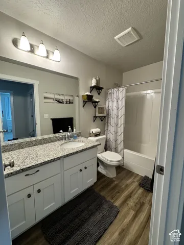 Bathroom featuring white cabinetry, stone-finish countertop with an integrated basin, wood-finish flooring, and a tub-shower combination