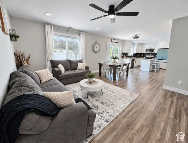 Open-concept interior featuring wood-finish flooring, recessed lighting, a modern ceiling fan, white kitchen cabinetry, and sliding glass patio doors