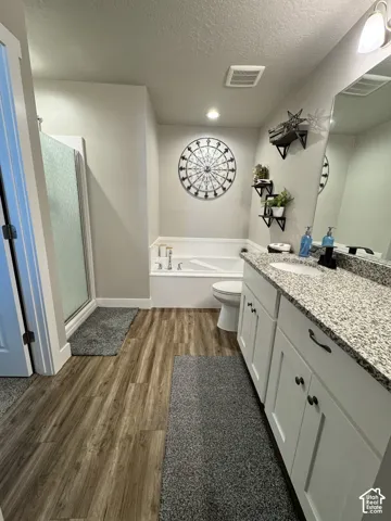 Bathroom featuring a vanity with a stone-composite countertop, drop-in sink, and white cabinetry, a separate soaking tub, and a shower enclosure with a glass door, finished with wood-finish flooring