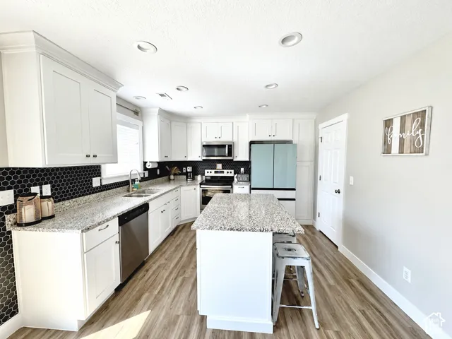 Kitchen featuring white shaker-style cabinetry, stone-surface countertops, central island, black hexagonal tile backsplash, and wood-finish flooring