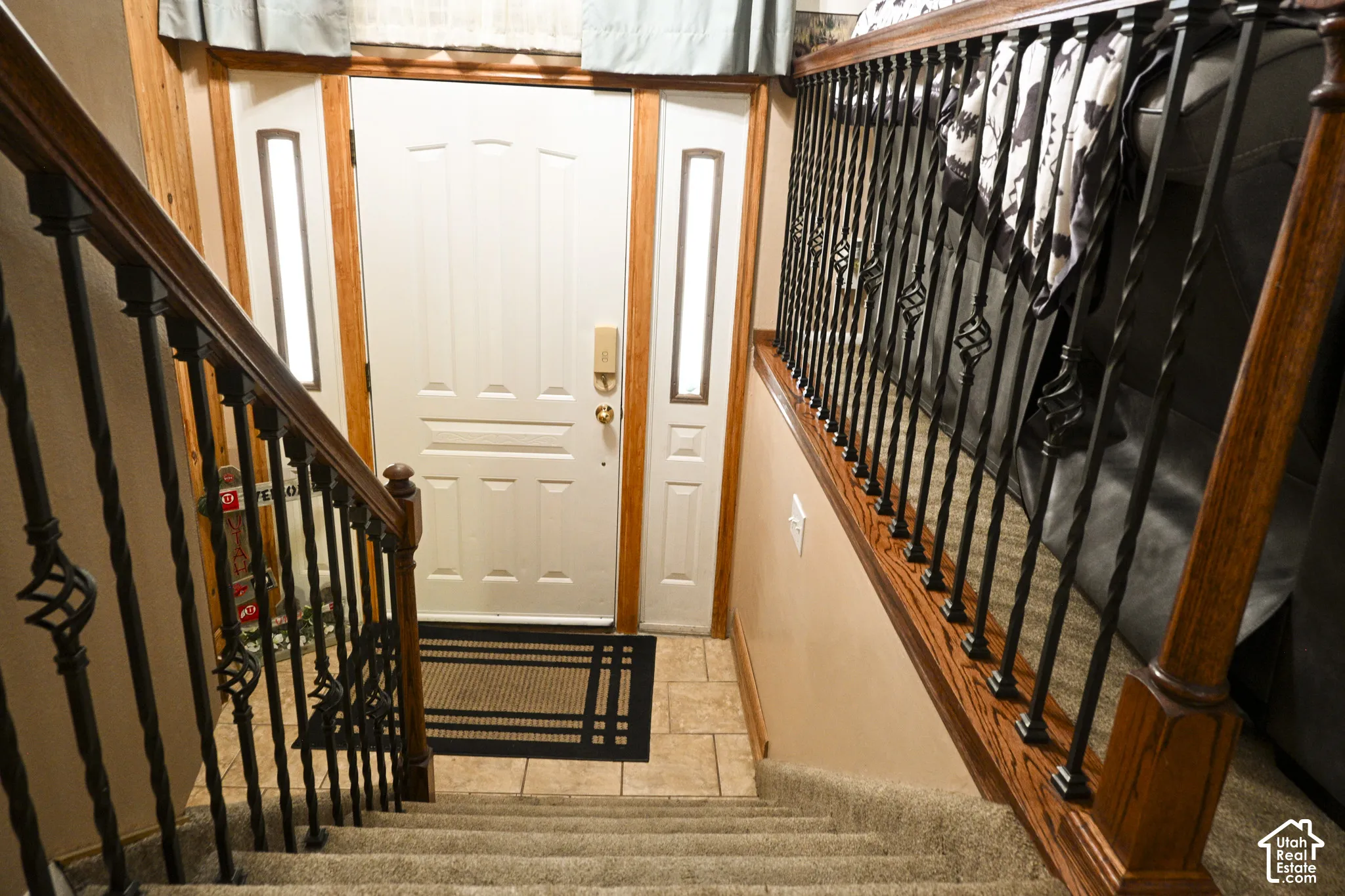 Entryway featuring a white paneled door with side lights, tile flooring, and a staircase with stained wood handrails and black metal balusters