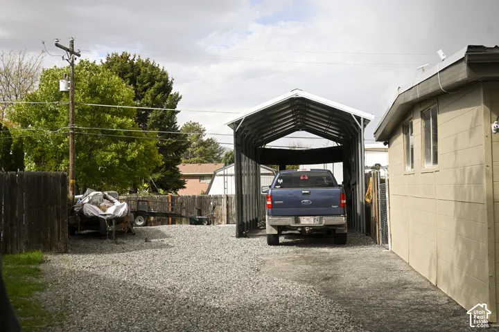 Gravel parking area featuring a detached metal carport and wood fencing
