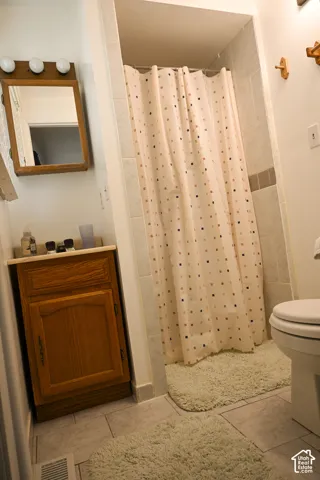 Bathroom featuring a wood vanity, recessed shower enclosure with tiled surround, wall-mounted mirror with integrated lighting, and ceramic tile flooring