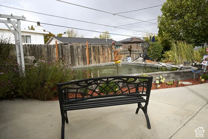 Outdoor space featuring a stone-retaining wall water feature, concrete patio, white-painted wood pergola, and wood privacy fencing