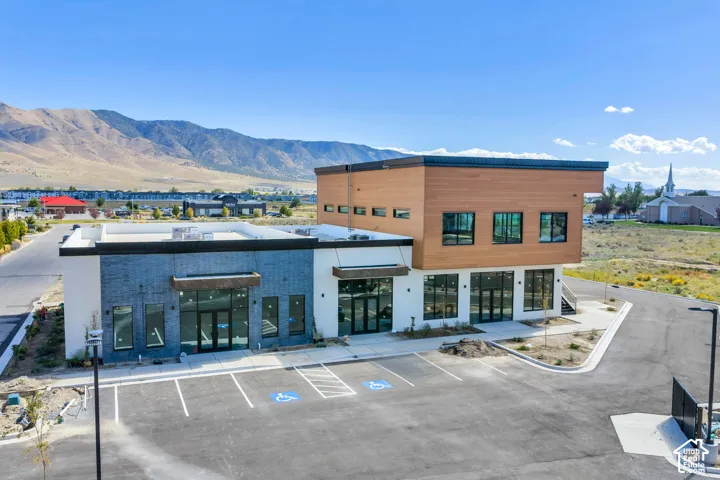 Modern commercial property exterior featuring horizontal wood siding, dark brick and white stucco facade, expansive glass storefronts, and an on-site asphalt parking area with mountain backdrops