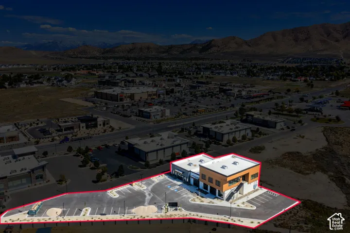 Two-story commercial building featuring a flat roof, exterior staircase, multi-tenant entrances, paved parking lot, and mountain scenery