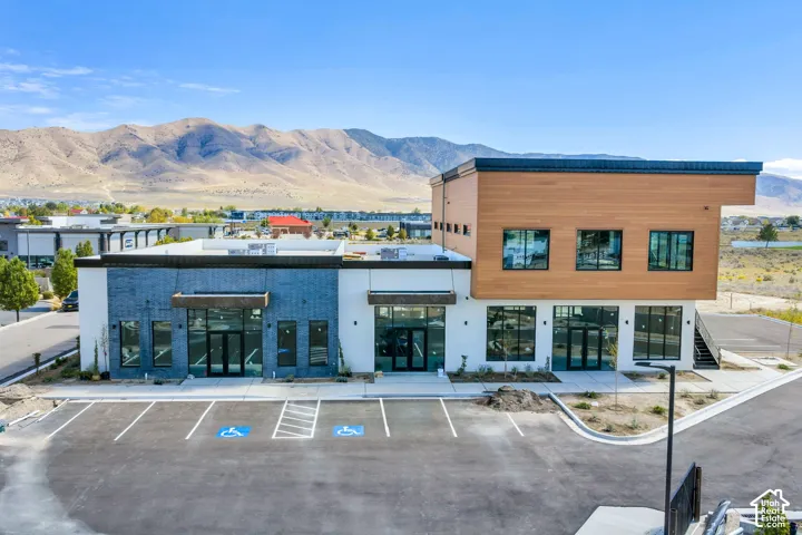 Commercial building exterior featuring two-tone brick and smooth-finish siding, flat roofline, floor-to-ceiling glass storefront entries, paved parking lot, and mountain scenery