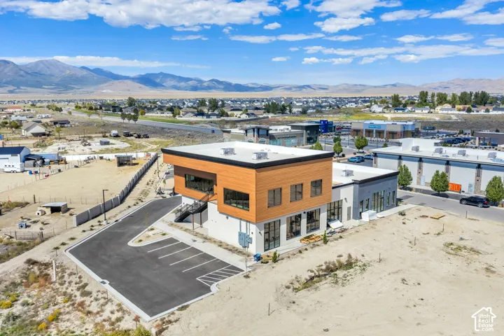 Two-story commercial building featuring wood-composite cladding, white smooth-finish exterior, expansive windows, paved parking area, and mountain range backdrop
