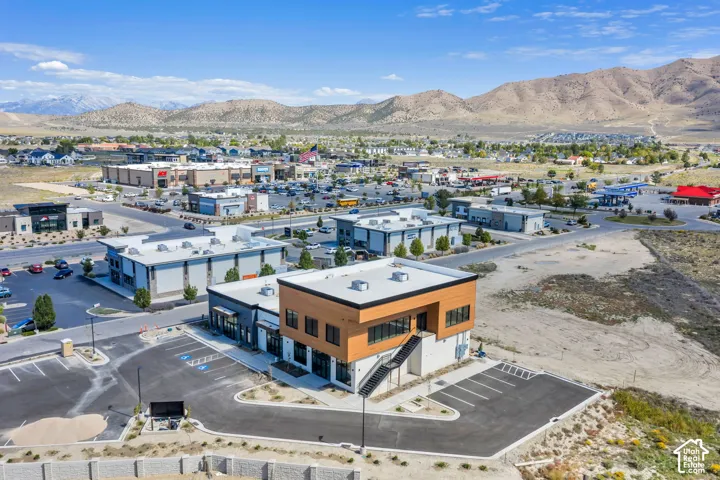 Two-story commercial building featuring wood-tone paneling, metal staircase, paved parking lot, and mountain backdrop