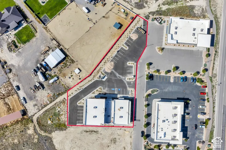 Aerial perspective of the property featuring a paved asphalt parking area, clearly defined lot boundaries, dual commercial structures with flat roofs, and multiple marked parking stalls