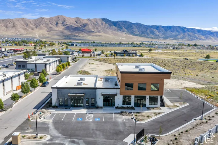 Contemporary multi-level structure featuring a wood-toned upper facade, flat roofline, paved parking area, and mountain range backdrop