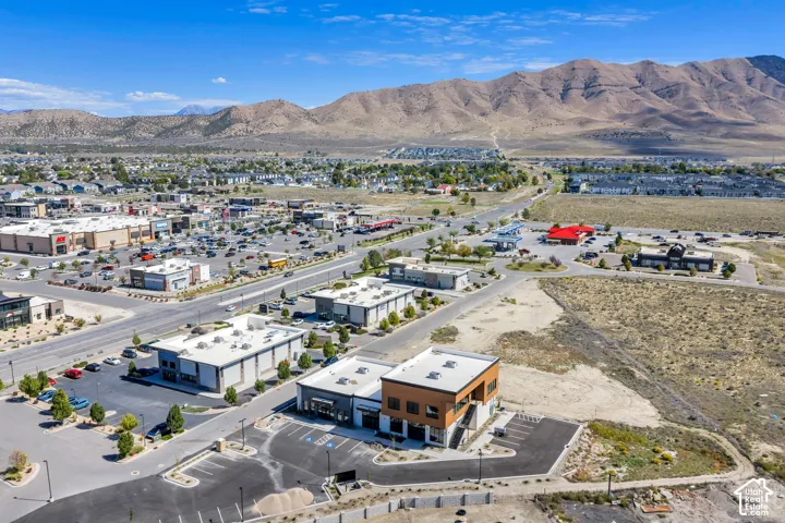 Aerial perspective featuring modern multi-tenant commercial structures, paved surface parking lots, and a backdrop of mountainous terrain