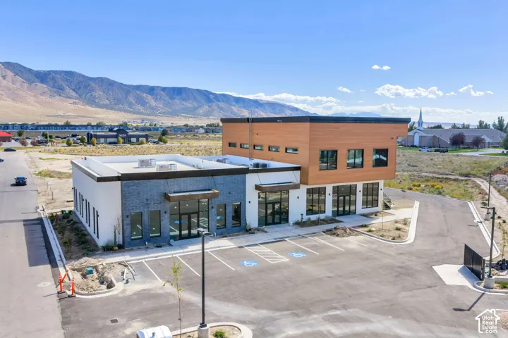 Commercial property featuring a mixed-material exterior of dark brick, light stucco, and wood-finish siding, accented by extensive glazing, a paved parking area, and a mountain backdrop