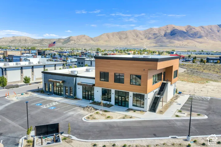 Multi-level commercial structure featuring wood-finish siding, white masonry accents, expansive glass storefronts, exterior metal staircase, and a dedicated asphalt parking lot against a mountain backdrop