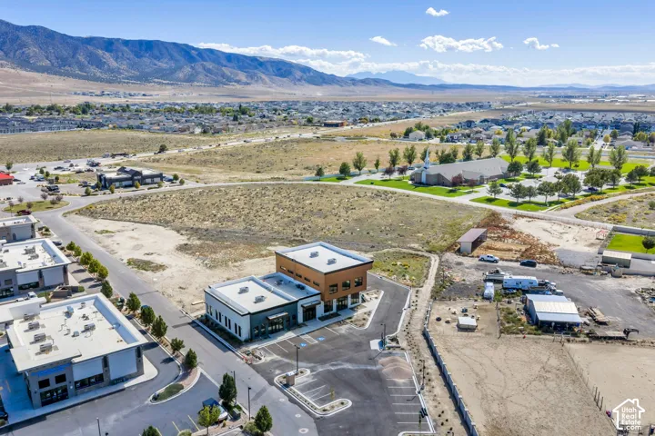 Aerial perspective of a multi-level commercial property featuring modern flat-roof architecture, wood-tone paneling, integrated asphalt parking, and expansive mountain range surroundings