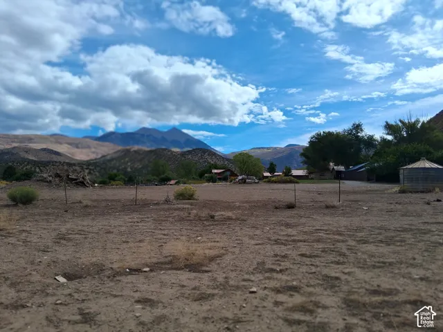 Expansive lot featuring wire fencing, mature trees, and a mountain backdrop