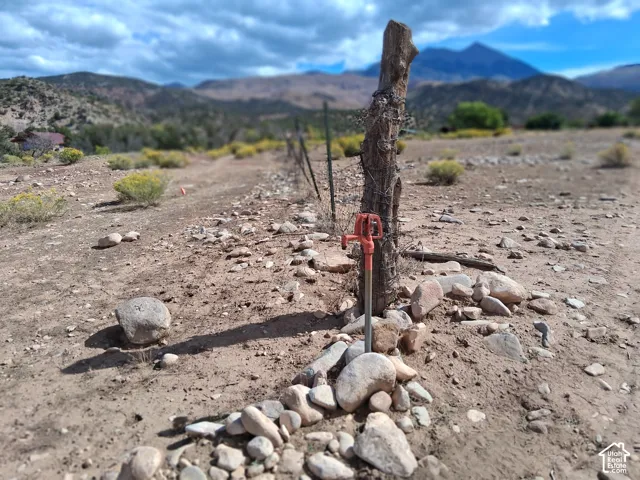 Exterior water hydrant with metal post and wire fencing set against a mountain backdrop